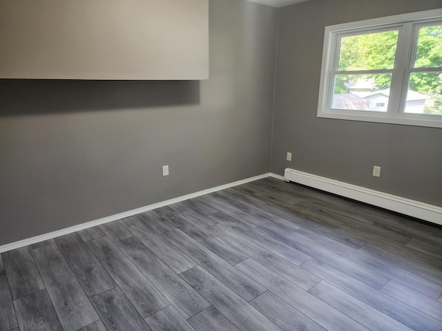 empty room featuring dark wood-type flooring, baseboard heating, and baseboards