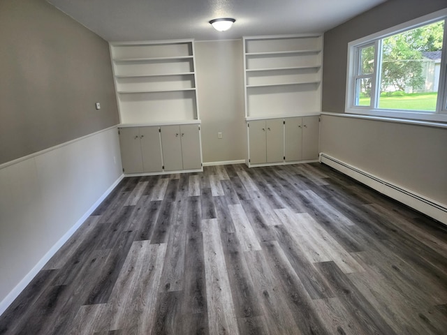 empty room with a baseboard heating unit, baseboards, built in features, and dark wood finished floors