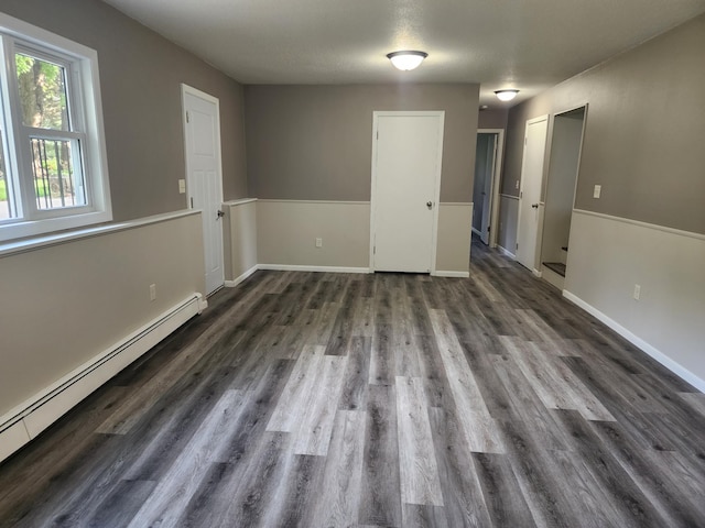 empty room featuring baseboard heating, wood finished floors, and baseboards