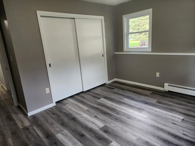 unfurnished bedroom with a baseboard heating unit, a closet, wood finished floors, and baseboards