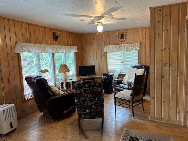 living room with ceiling fan, light wood-type flooring, and wooden walls