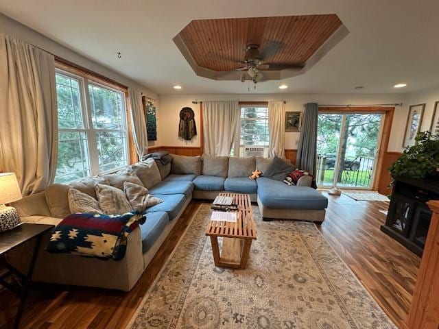 living room with hardwood / wood-style flooring, wooden walls, a raised ceiling, and ceiling fan