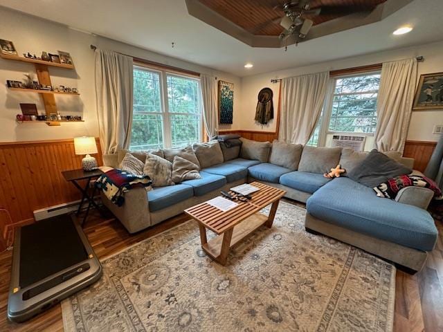 living room featuring hardwood / wood-style floors, wood walls, ceiling fan, a tray ceiling, and wooden ceiling