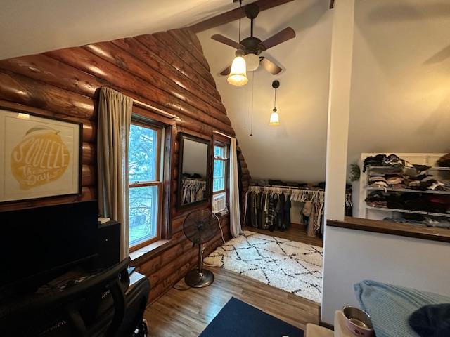 interior space featuring vaulted ceiling, wood-type flooring, log walls, and ceiling fan