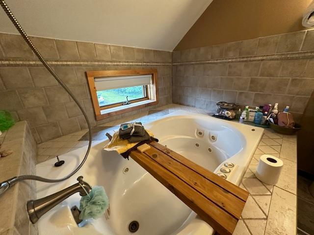 bathroom with a relaxing tiled tub, tile patterned floors, lofted ceiling, and tile walls