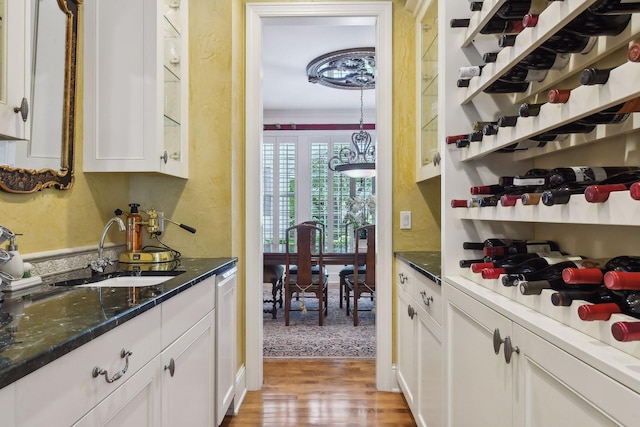 interior space featuring dark stone counters, sink, ornamental molding, light wood-type flooring, and white cabinetry