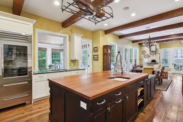 kitchen featuring butcher block counters, an inviting chandelier, a kitchen island with sink, wood-type flooring, and hanging light fixtures