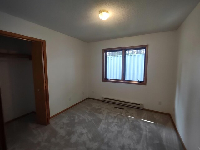 unfurnished bedroom with a closet, a textured ceiling, a baseboard radiator, and dark carpet