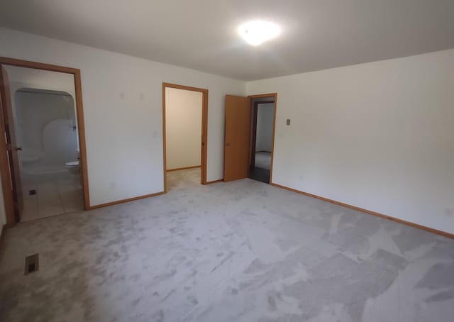 unfurnished bedroom with a closet, ensuite bathroom, and light carpet