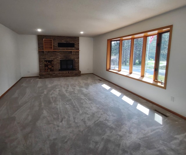 unfurnished living room featuring carpet flooring, a textured ceiling, and a brick fireplace