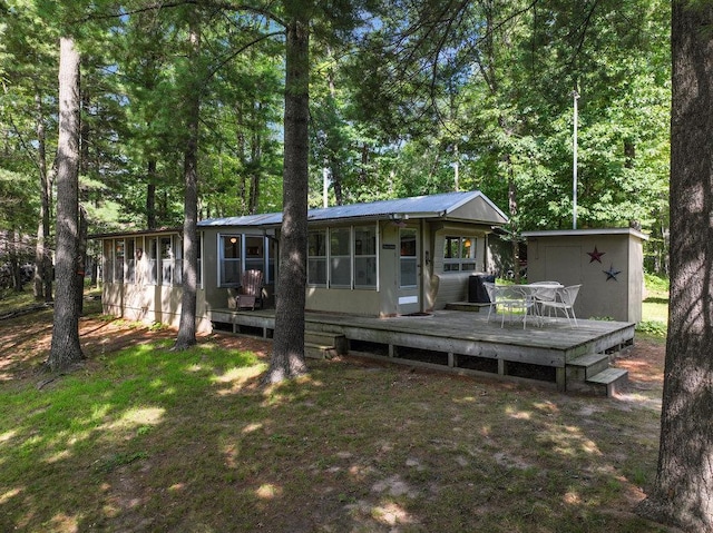 rear view of property with a sunroom, a deck, and a lawn