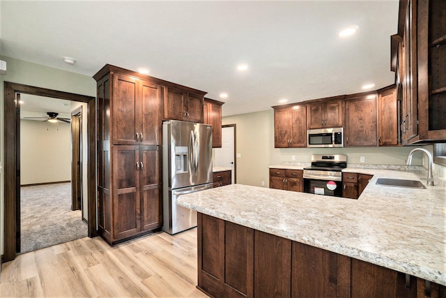 kitchen featuring light wood finished floors, stainless steel appliances, light countertops, a sink, and a peninsula