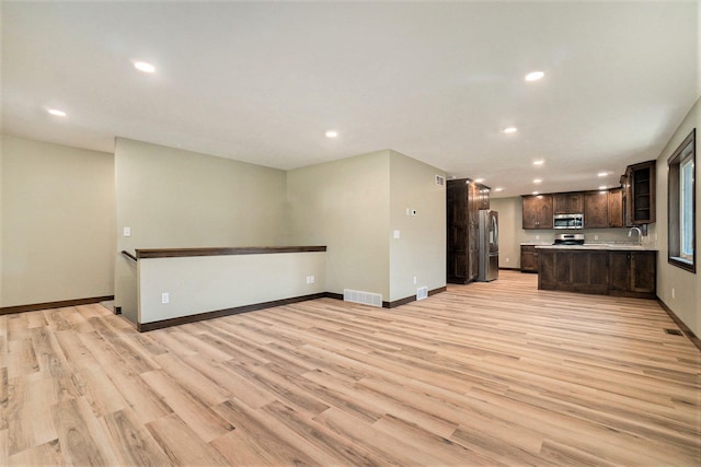 kitchen featuring stainless steel appliances, light countertops, visible vents, open floor plan, and dark brown cabinetry