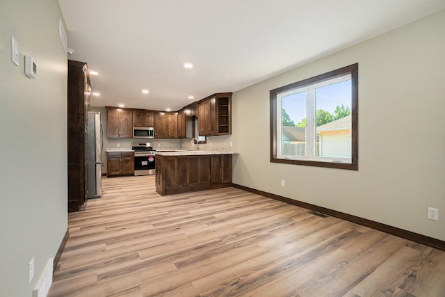 kitchen with dark brown cabinetry, stainless steel appliances, a sink, baseboards, and light countertops