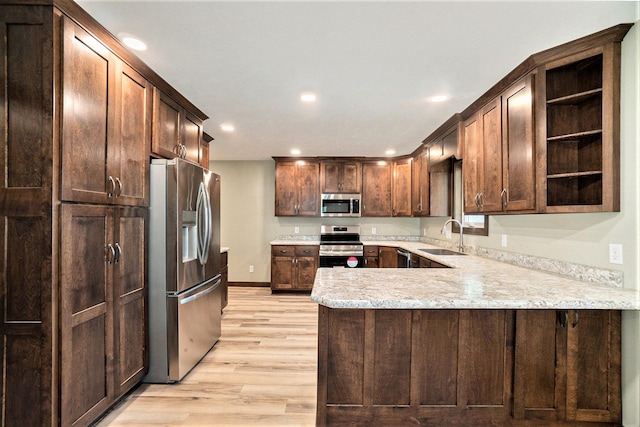 kitchen featuring light wood finished floors, appliances with stainless steel finishes, a peninsula, open shelves, and a sink