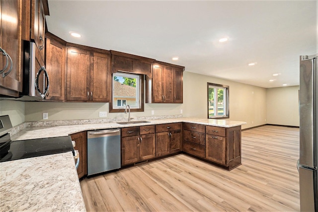 kitchen featuring a peninsula, light wood-style floors, appliances with stainless steel finishes, and a sink