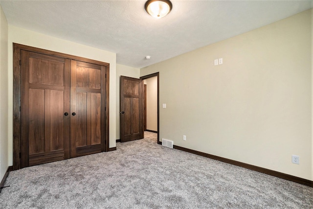 unfurnished bedroom with a textured ceiling, light colored carpet, visible vents, baseboards, and a closet