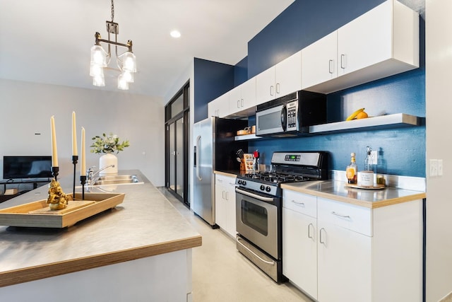 kitchen featuring a notable chandelier, hanging light fixtures, stainless steel appliances, sink, and white cabinets