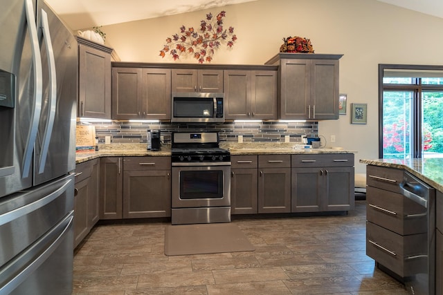 kitchen featuring appliances with stainless steel finishes, lofted ceiling, decorative backsplash, and light stone countertops