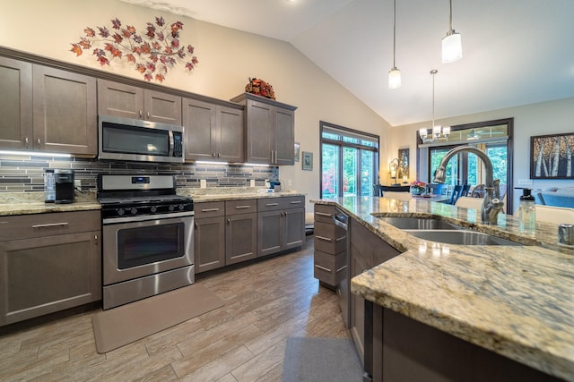 kitchen with stainless steel appliances, light wood-style flooring, decorative backsplash, a sink, and light stone countertops