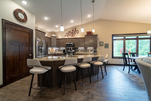 kitchen with a breakfast bar, stainless steel appliances, tasteful backsplash, vaulted ceiling, and dark brown cabinetry