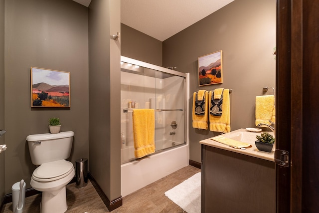 bathroom with baseboards, shower / bath combination with glass door, vanity, and toilet