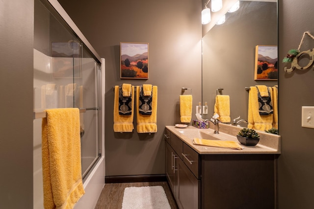 full bath with bath / shower combo with glass door, wood finished floors, and vanity