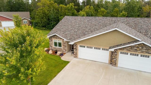 view of front facade with concrete driveway, stone siding, roof with shingles, an attached garage, and a front yard