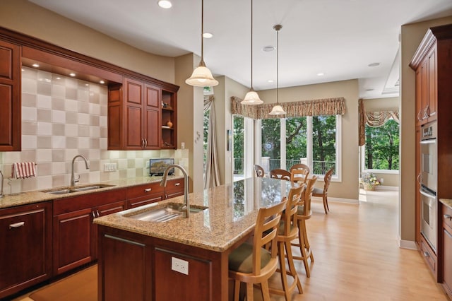 kitchen featuring an island with sink, sink, hanging light fixtures, and backsplash