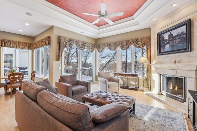 living room with light hardwood / wood-style flooring, ornamental molding, a raised ceiling, ceiling fan, and a tiled fireplace