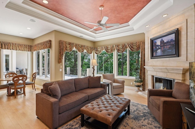 living room with crown molding, a tray ceiling, a high end fireplace, and a healthy amount of sunlight