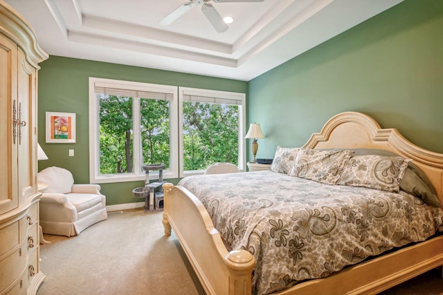 bedroom featuring a raised ceiling, light carpet, and ceiling fan