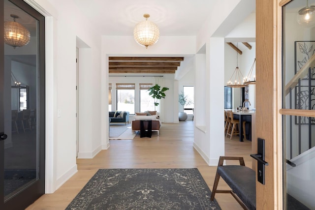 entrance foyer featuring beamed ceiling, a chandelier, and light hardwood / wood-style floors