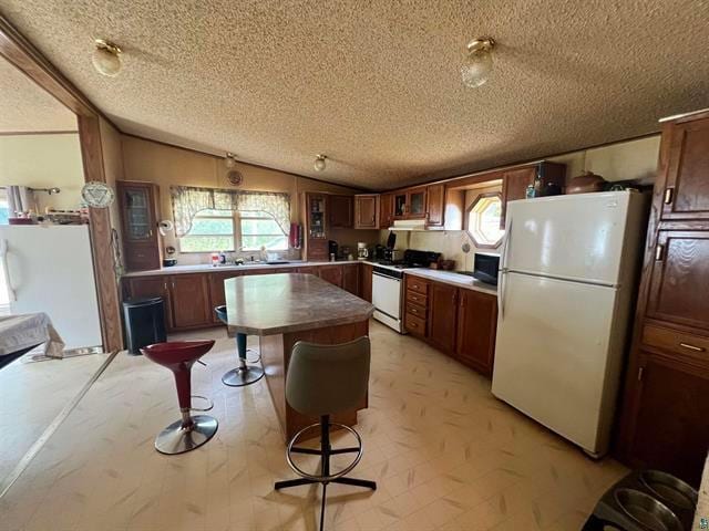 kitchen featuring sink, white appliances, a textured ceiling, and lofted ceiling