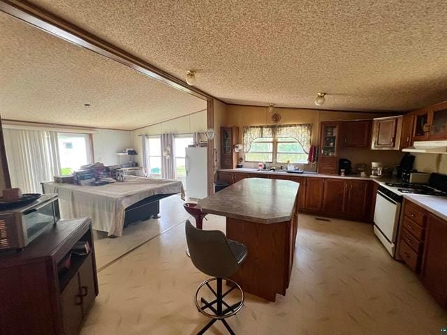 kitchen with a textured ceiling, lofted ceiling, white range oven, light carpet, and a kitchen island