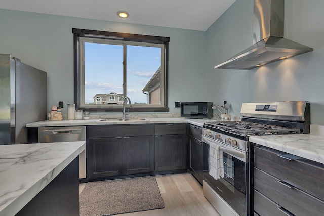 kitchen featuring wall chimney exhaust hood, appliances with stainless steel finishes, light stone counters, light hardwood / wood-style floors, and sink