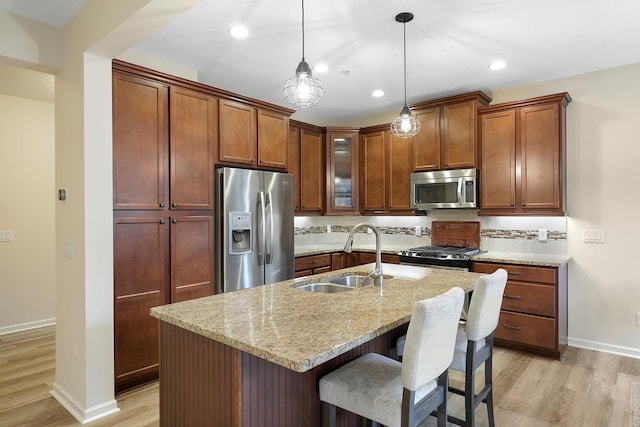 kitchen with sink, light wood-type flooring, stainless steel appliances, light stone countertops, and a kitchen island with sink