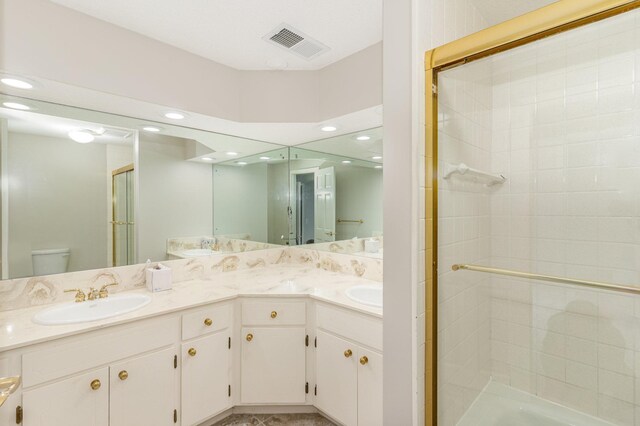 full bathroom with visible vents, toilet, a sink, a shower stall, and double vanity