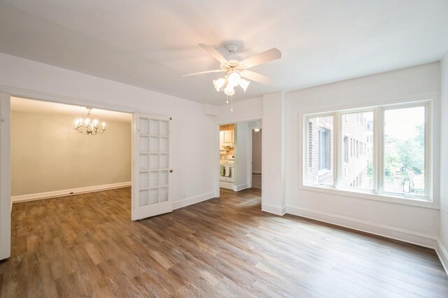 spare room with ceiling fan with notable chandelier, wood finished floors, and baseboards