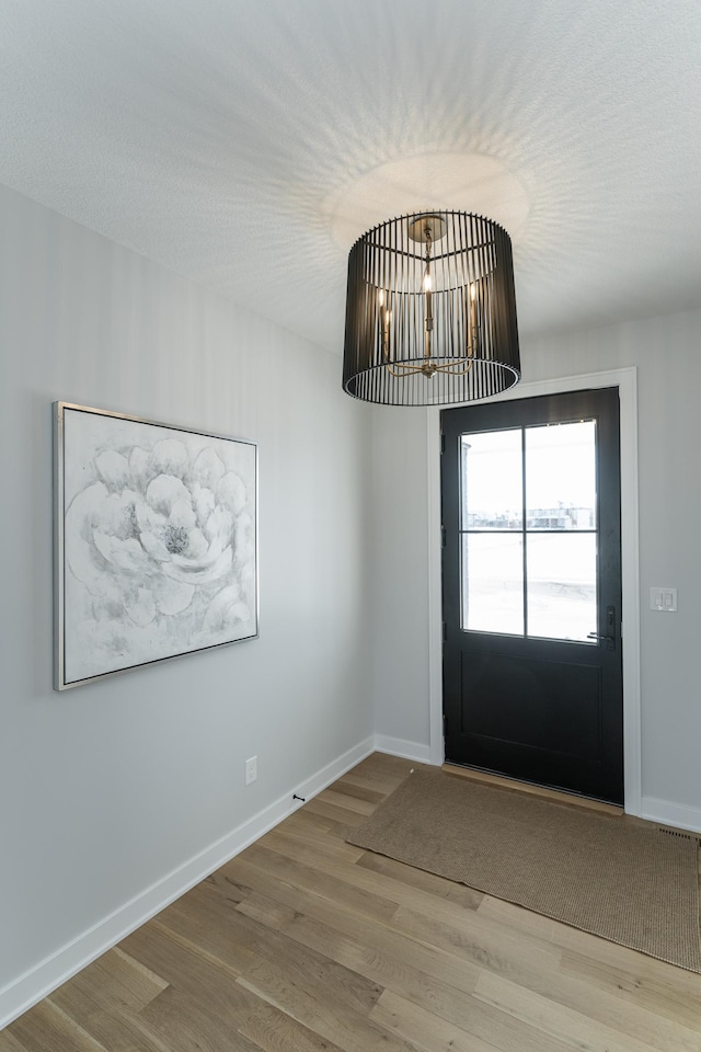 interior space featuring a chandelier, a textured ceiling, wood finished floors, and baseboards