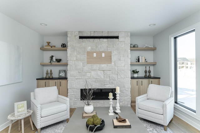 living area with a healthy amount of sunlight, a stone fireplace, baseboards, and wood finished floors