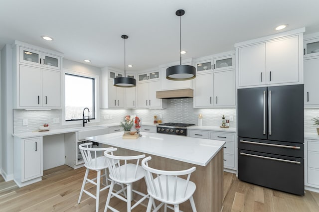 kitchen featuring high end black refrigerator, a kitchen island, white cabinetry, light countertops, and glass insert cabinets