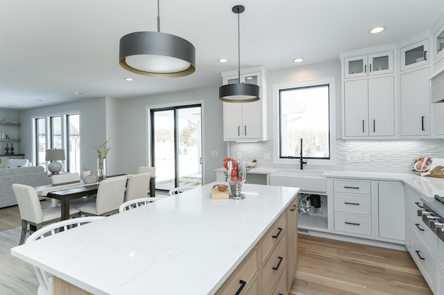 kitchen featuring a center island, decorative light fixtures, glass insert cabinets, open floor plan, and white cabinetry