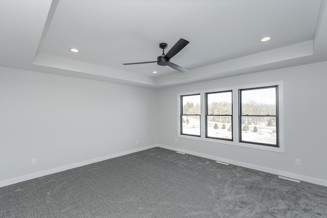 empty room featuring ceiling fan, recessed lighting, baseboards, dark colored carpet, and a tray ceiling