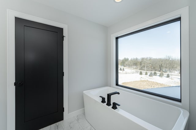 bathroom with marble finish floor, a freestanding bath, and baseboards