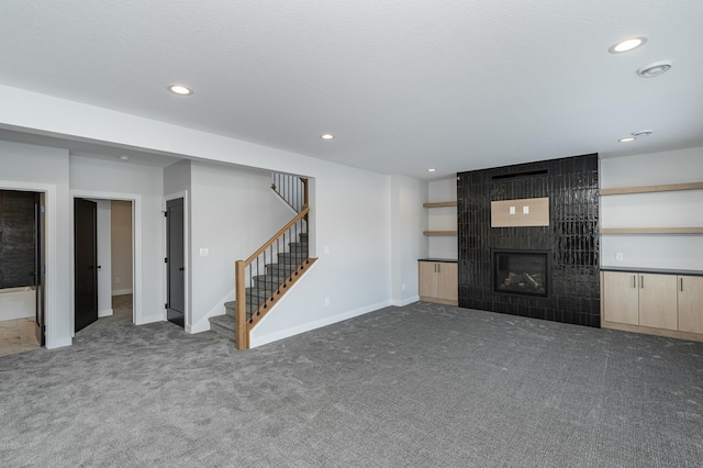 unfurnished living room featuring a large fireplace, stairs, carpet flooring, and recessed lighting