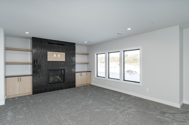 unfurnished living room featuring dark carpet, recessed lighting, a tiled fireplace, and baseboards