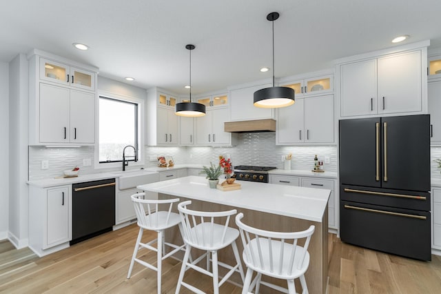 kitchen featuring high end black refrigerator, dishwashing machine, light wood-style flooring, white cabinetry, and a sink