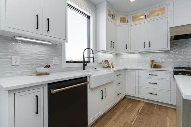 kitchen featuring decorative backsplash, light wood-style flooring, black dishwasher, and a sink
