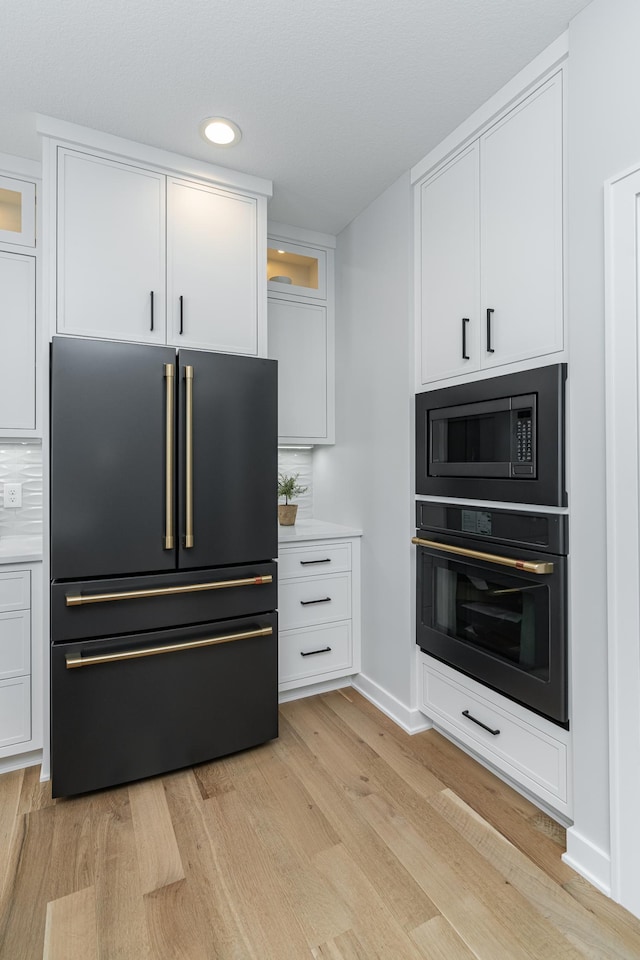 kitchen featuring white cabinetry, black appliances, light wood-style floors, and light countertops